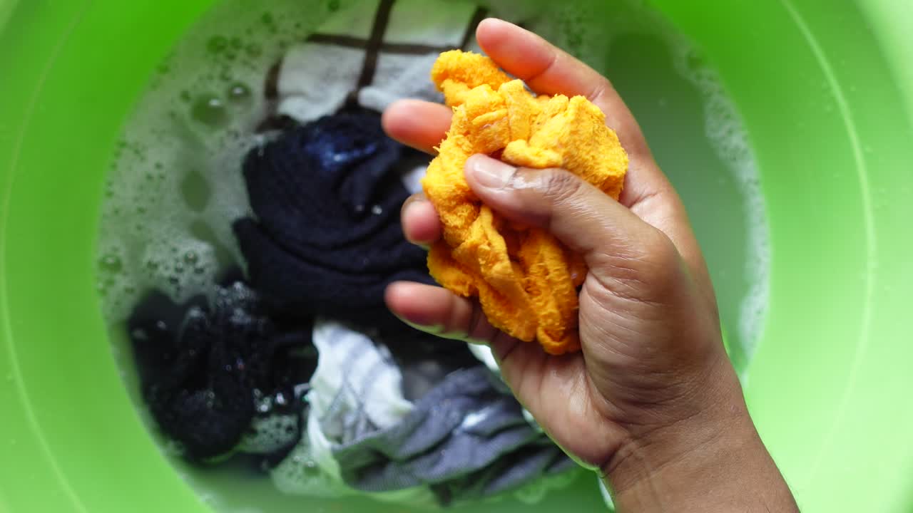 una mano lavando la ropa en un cubo verde