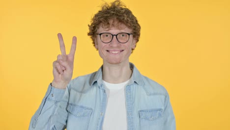 signo de victoria por un joven pelirrojo, fondo amarillo