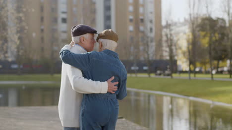 Elderly-Couple-Dancing-At-Pier-In-City-Park-On-Warm-Autumn-Day-With-Multi-Storey-Buildings-In-Background