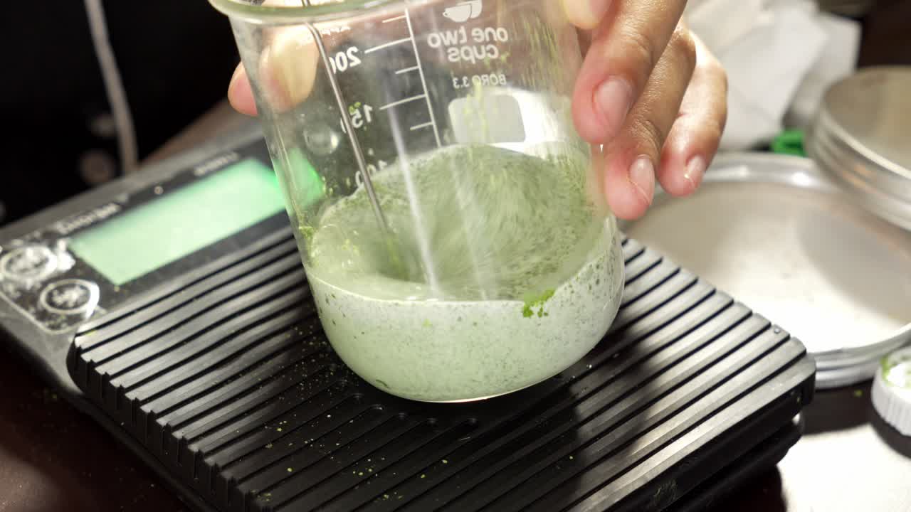 Dettaglio ravvicinato di miscela di polvere di matcha con latte in becher di vetro su bilancia digitale per la preparazione del tradizionale latte matcha giapponese