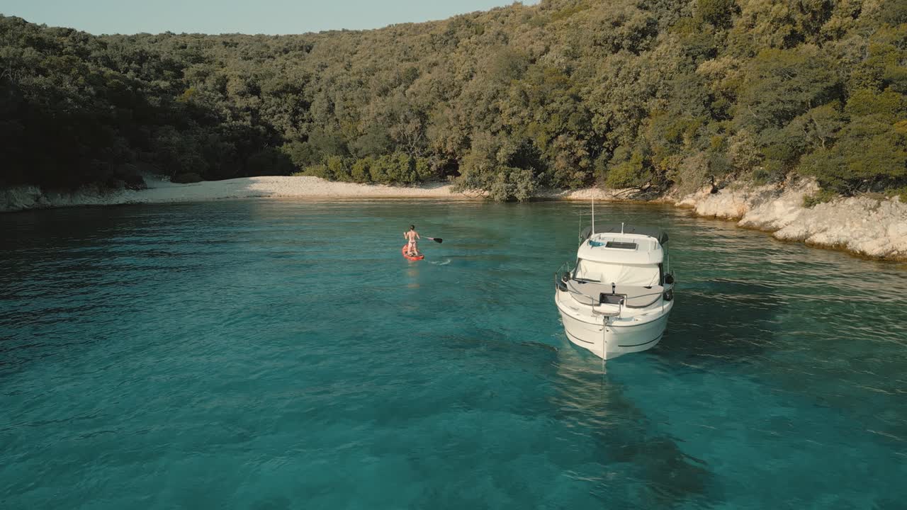 A person on a stand-up paddleboard and a boat anchored in the tranquil Perla Bay