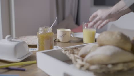 man's hands serving nutritious breakfast with bread, jam and orange juice on table