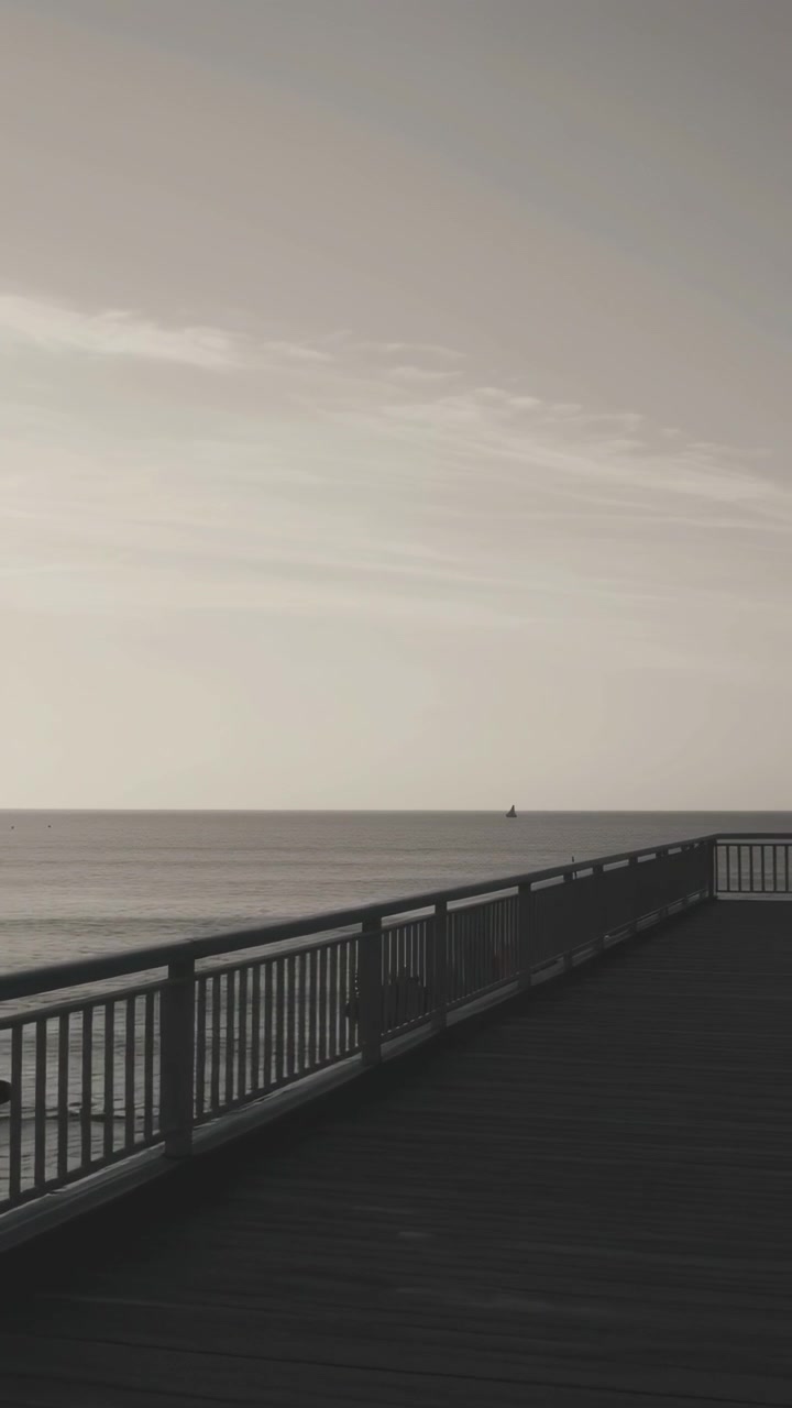 Calm Ocean View from a Pier with a Sailboat in Sepia Tone