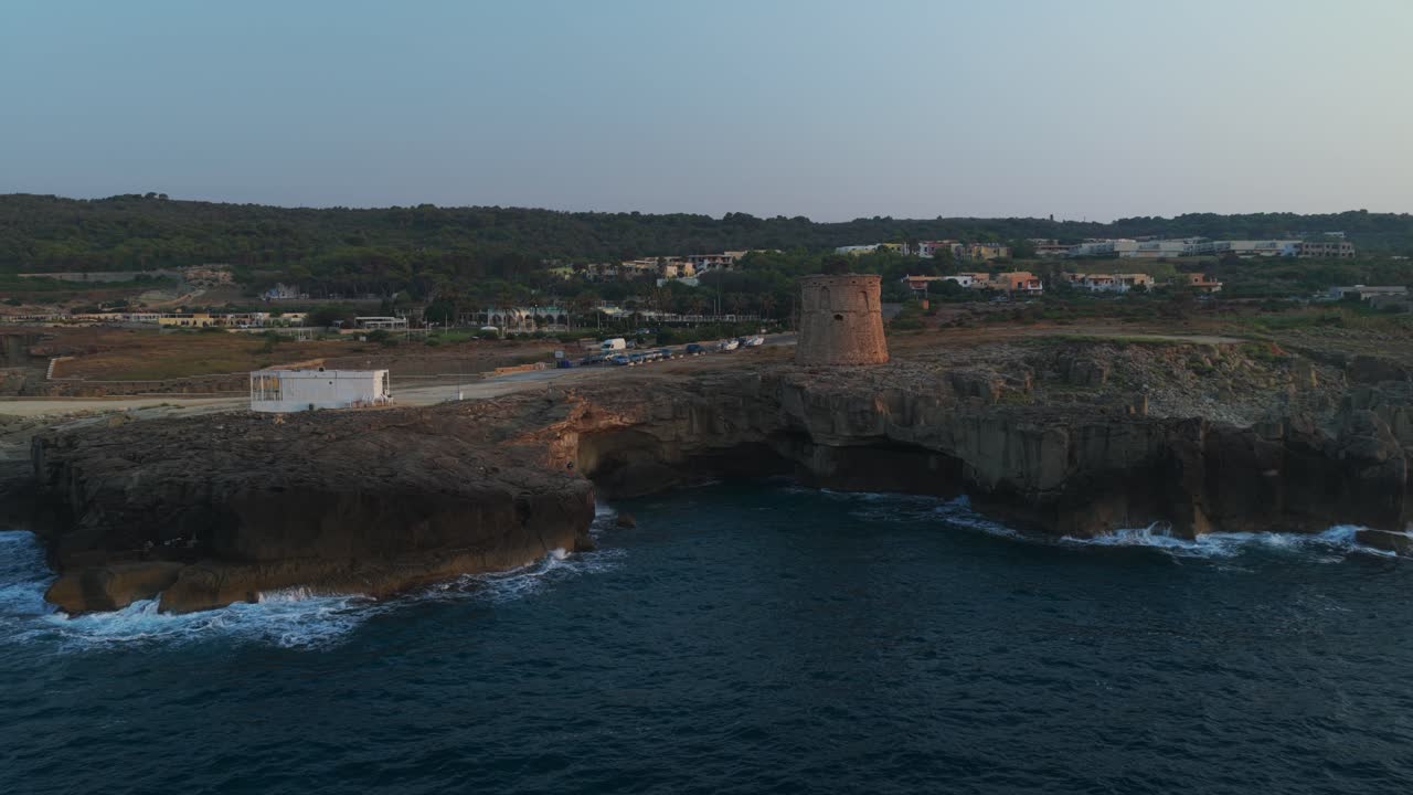 Torre de vigia histórica em Porto Miggiano, Puglia, penhascos escarpados, ondas quebrando e luz dourada do pôr do sol, Itália. Aéreo para trás