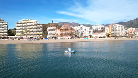 Aerial-dolly-over-boat-dragging-nets-in-water-with-ocean-view-hotels-behind