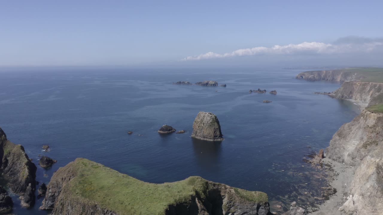 sobrevuelo aéreo de rocas apiladas en el mar frente a la escarpada costa del océano en calma