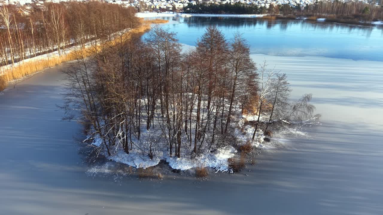 Droneopptak fra luften som sirkler rundt en liten, tredekket øy om vinteren. Nedfalne blader, snødekt bakke og rolig dagslys skaper et stille, filmatisk landskap i den kalde årstiden.