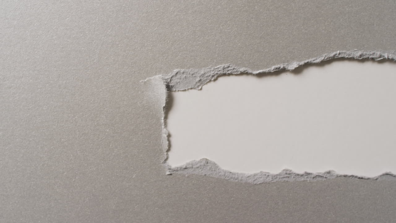 Video of close up of torn grey paper on white background