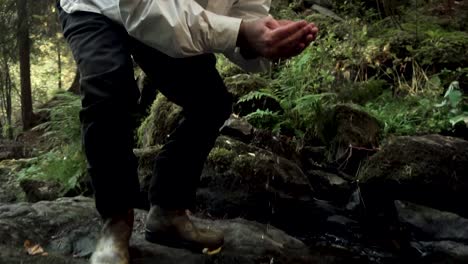 person drinking water from a stream in the forest