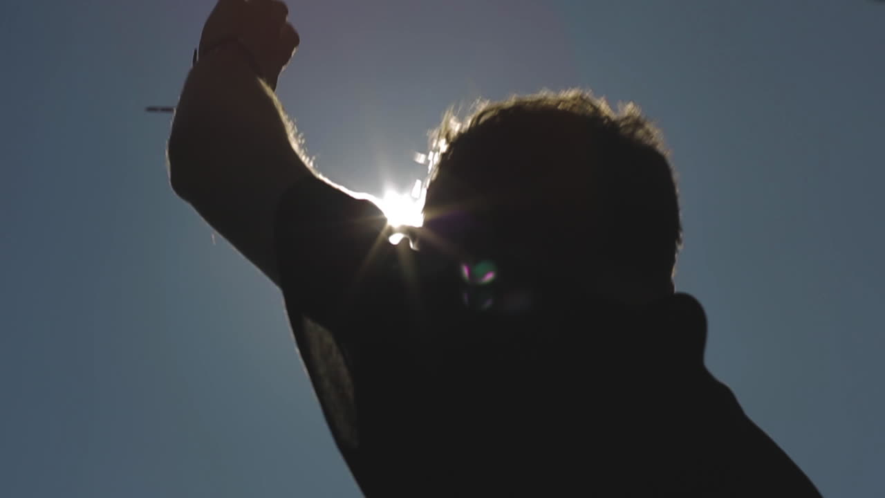 DJ in the sunshine. Outdoors a musical producer plays electronic music and waits for the drop to sound. Sun rays fall from the sky creating his silhouette