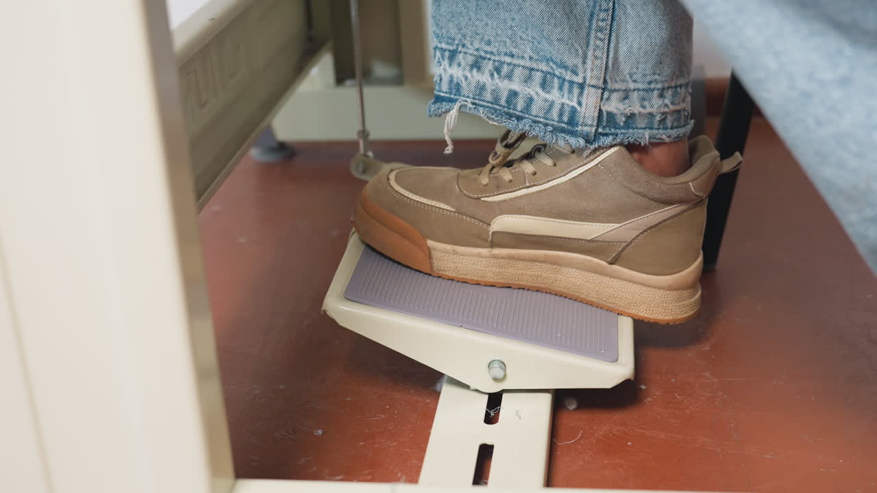 Foot pedal being stepped on by female foot wearing canvas shoes, controlling machine speed, demonstrating professional skill, ensuring accurate adjustments, highlighting mechanical process