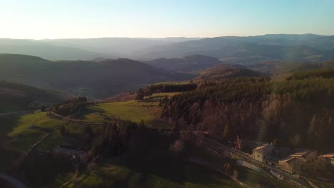 Vista-De-Drones-De-La-Campiña-Francesa-Con-Bosques,-Colinas-Y-Pueblo-En-Ardèche-Bajo-La-Puesta-De-Sol