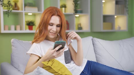 Young-woman-sitting-at-home-dancing-and-looking-at-her-phone.