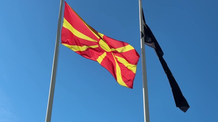 Nationalflagge von Nordmazedonien weht vor blauem Himmel mit rot-gelbem Sonnendesign