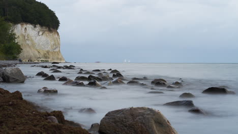 Zeitraffer-Von-Menschen,-Die-Touristen-Entlang-Der-Weißen-Kreidefelsen-Auf-Der-Insel-Rügen-Spazieren,-Während-Die-Wellen-Der-Ostsee-über-Den-Steinigen-Strand-Rollen