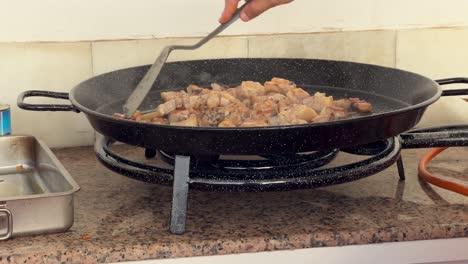 persona está fritando carne en un plato grande y preparándose para llevarlos a otro cuenco de metal