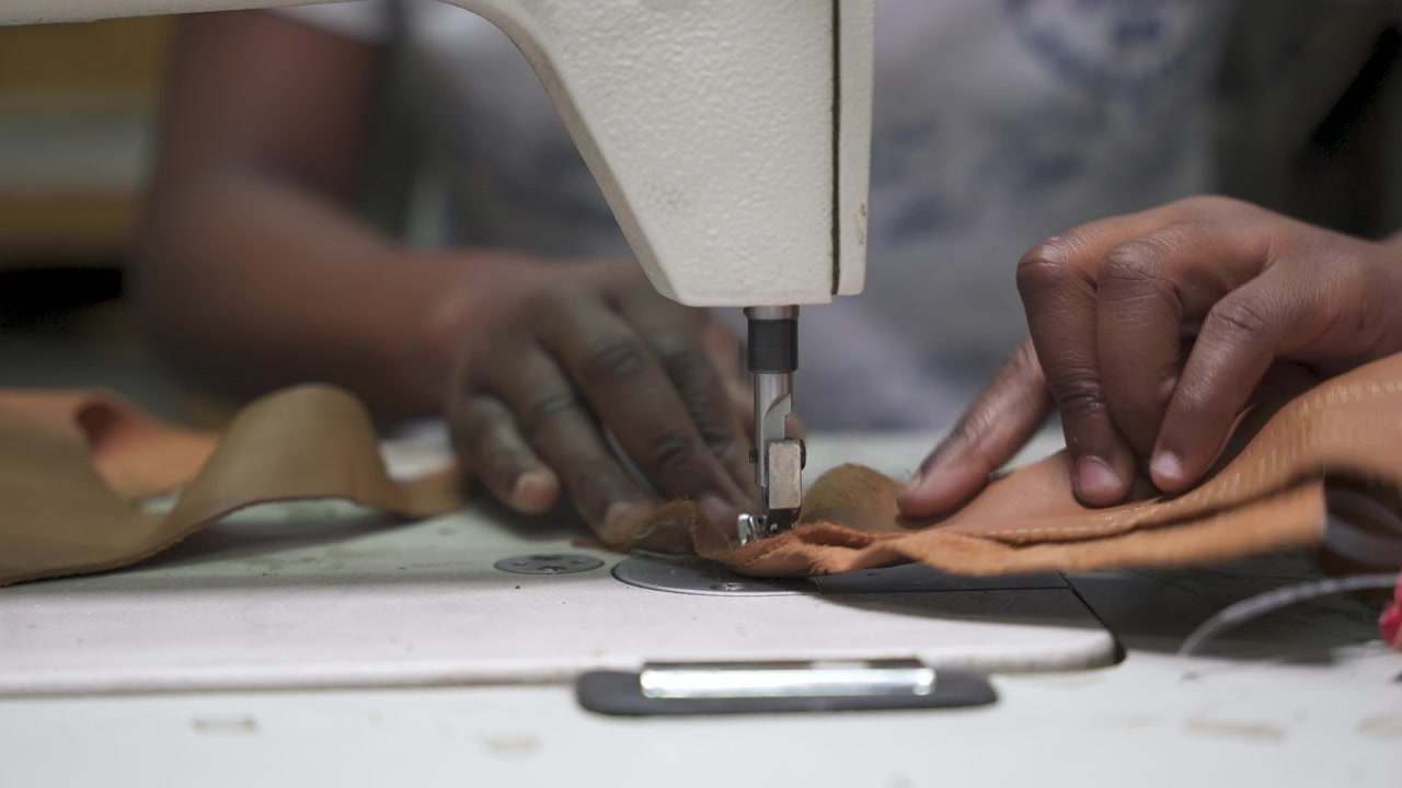 Close-up of hands expertly guiding leather under a sewing machine needle, capturing the precision of leather crafting. Suitable for artisan craft demonstrations or educational content.