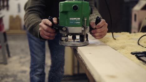 unrecognizable man carpenter working with handle grinding machine, polishing the wood bar. grinds a large wooden plank. slow motion