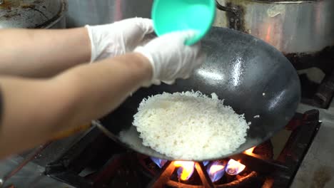 Cerca-De-Las-Manos-Del-Chef-Cocinando-Y-Tirando-Arroz-Blanco-Para-La-Cocina-Asiática-En-Una-Sartén-Wok-En-Una-Estufa-De-Gas.