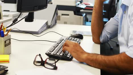 male executive using mobile phone while working on computer