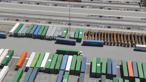 rows of shipping freight containers parked in a lot as truck repositions one - aerial view