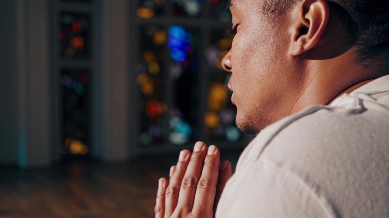Young Man Praying in a Church with Stained Glass Window