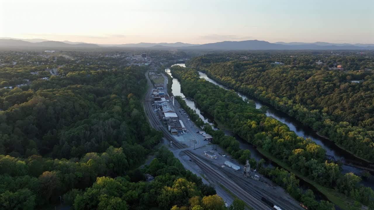 Suburb neighborhood with green trees near James River and railway tracks at sunset. Aerial flyover shot. Wide shot. Forest landscape in the evening. Sewage power plant in Lynchburg