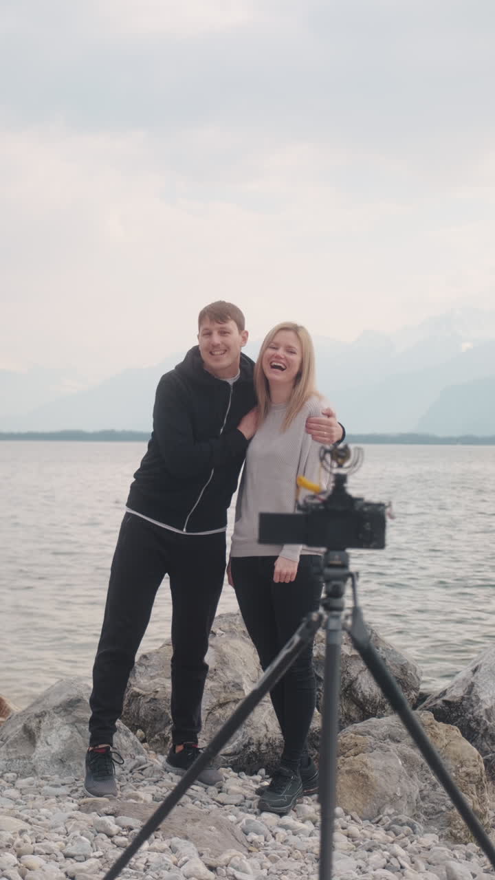Verticale: primo piano di una coppia caucasica che fa vlogging davanti a un treppiede con fotocamera e al Lago di Ginevra a Montreux, Svizzera, ripresa statica