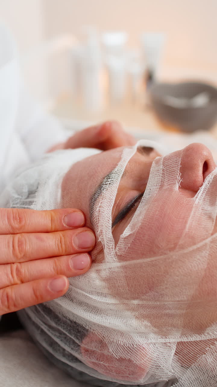 Woman completing facial wrap mask procedure in cosmetology clinic beautician apply gauze skin care