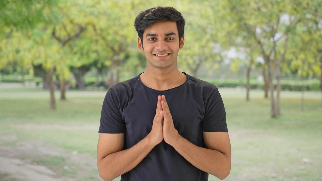 Cute Indian boy doing Namaste in a park