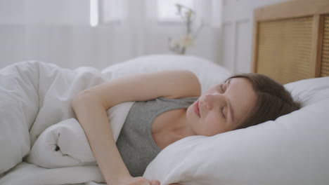 young woman laying in bed suffers from noise generated by the construction site outside the window. woman covering her ears with pillow.