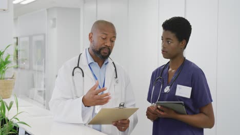 Afroamerikanische-Ärzte-Und-Ärztinnen-Halten-Klemmbrett-Und-Tablet-In-Der-Hand-Und-Reden-Im-Krankenhaus