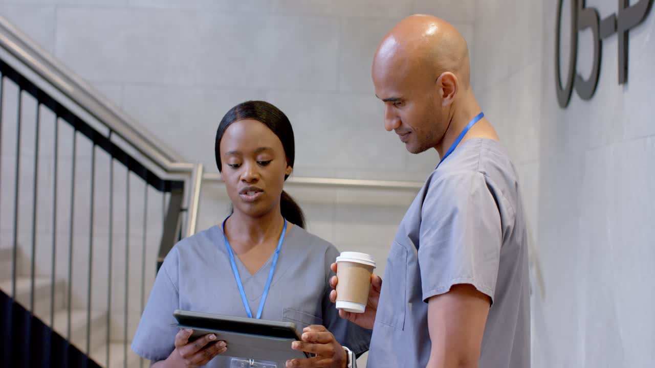Medical staff gesturing on stairs, woman tapping tablet checking chart while man holding coffee cup