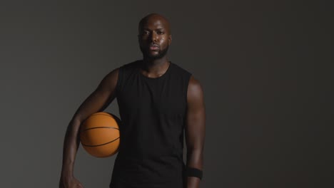retrato de estudio de un jugador de baloncesto que sostiene la pelota bajo el brazo contra un fondo oscuro