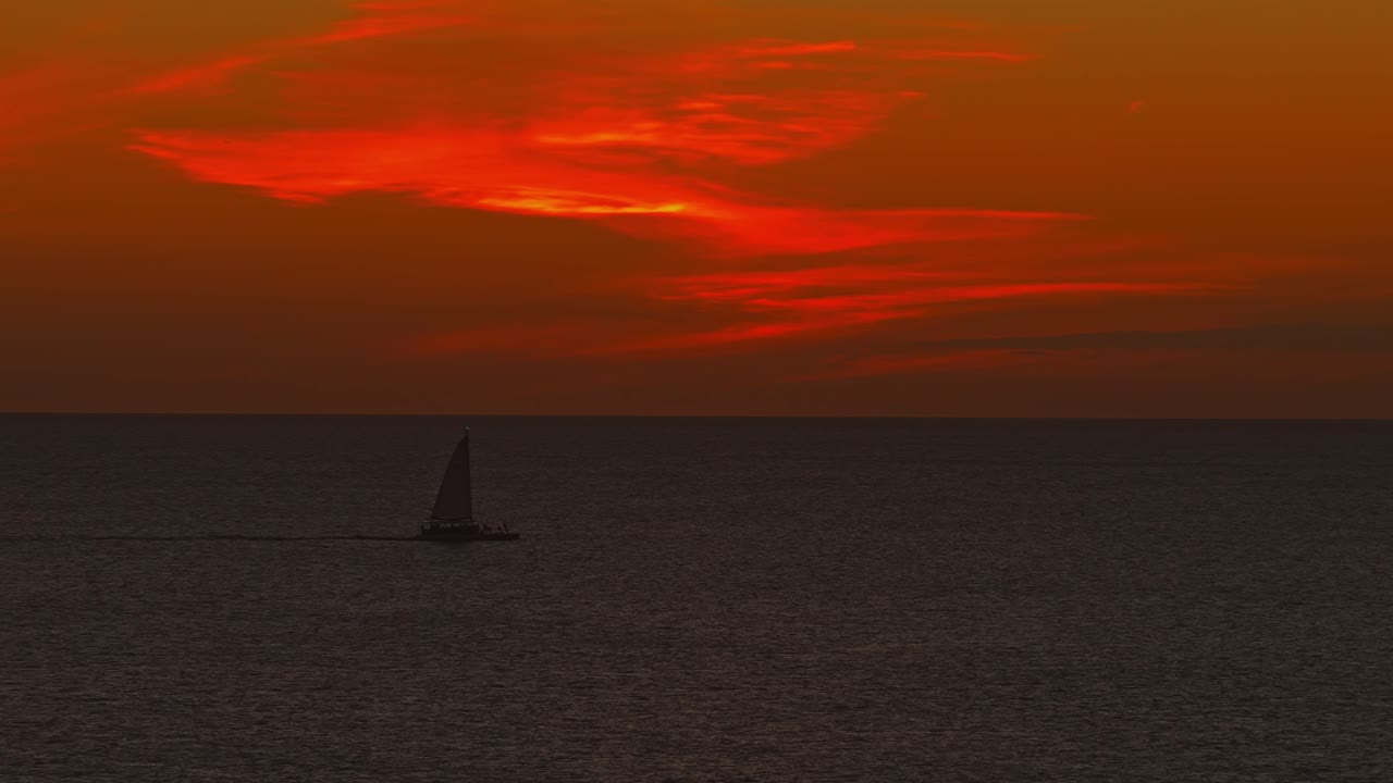 Segelboot auf dem Ozean bei Sonnenuntergang mit dramatisch rotem Himmel