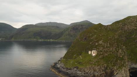 distant view of coastal hendanes lighthouse at the top of the cliff in vagsoy island, norway