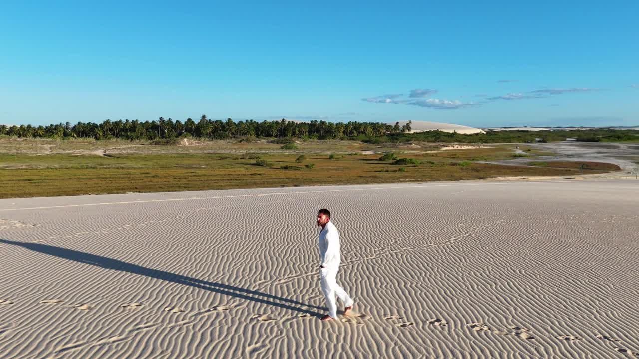 man dressed in a white outfit walking cinematically through the dunes