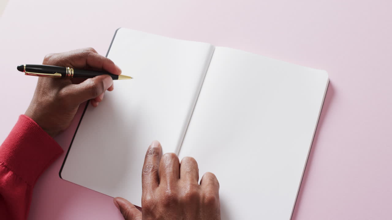 Close up of hands holding pen and blank pages of book, copy space on pink background, slow motion