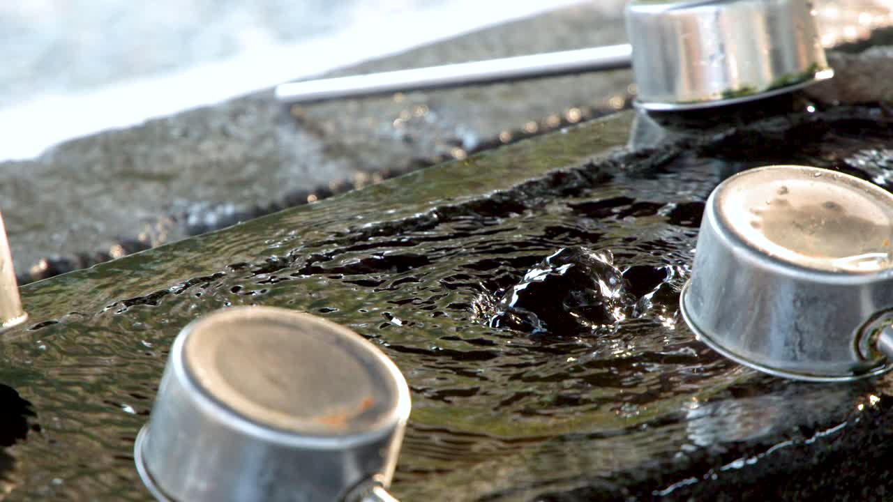 Primo piano di acqua che gorgoglia in una vasca di pietra con mestoli di metallo a Kanazawa.