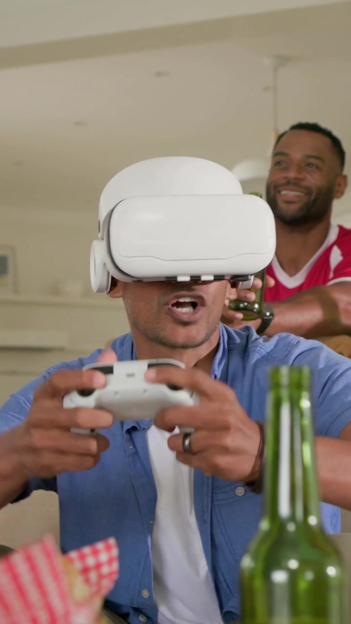 Vertical video: Game on, center man in blue shirt wearing headset using controller at home to play