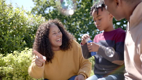 happy african american mother and father with son blowing bubbles in sunny garden