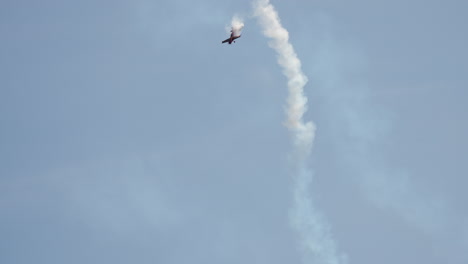 single airplane flies vertically with smoke trail behind while performing stunt during airshow