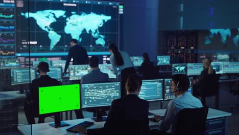 un equipo de ingenieros profesionales de ciencias de datos informáticos trabaja en escritorios en la sala de control y monitoreo. una pantalla tiene una maqueta de pantalla verde, otras muestran gráficos, gráficos y estadísticas técnicas.