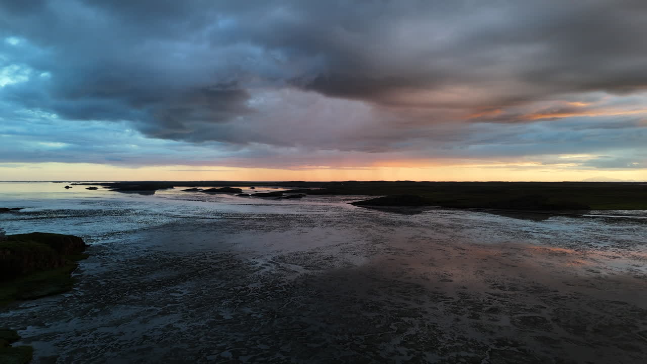 Aerial view of Borgarfjörður fjord near Borgarnes, Iceland at sunset, highlighting calm waters, warm orange sky, and surrounding mountains