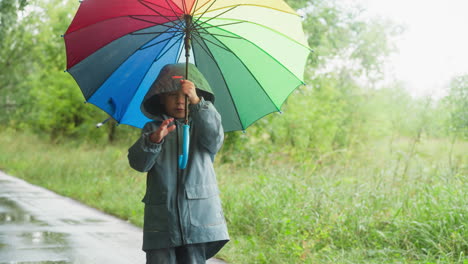 a little girl walks down a path in the rain, holding a rainbow umbrella