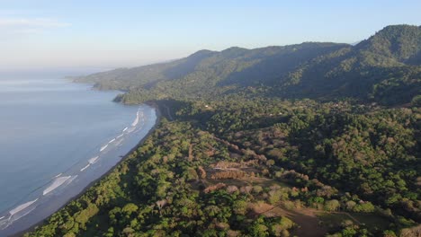 drone de costa rica volando sobre el denso bosque verde y las montañas en un día soleado con el mar pacífico en el lado