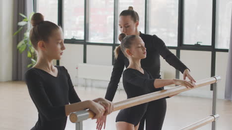 female teacher corrects the arm and leg position of the gymnastic girl in ballet class