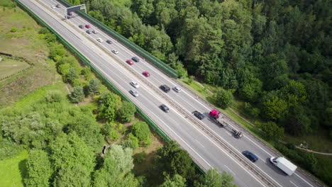 Vista-Aérea-De-Arriba-Hacia-Abajo-Del-Tráfico-Fluido-De-Automóviles-Y-Camiones-En-La-Carretera-Rural-De-Varios-Carriles-En-La-Región-De-Gdynia,-Polonia,-Rodeada-De-Campos,-Tierras-Verdes,-árboles-Y-Casas-Suburbanas,-Viajes-Y-Transporte