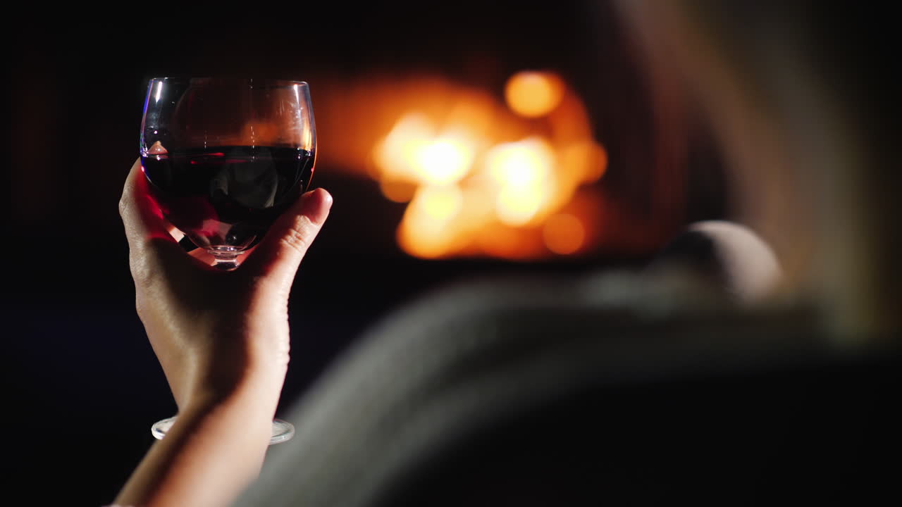 벽난로 후면보기 옆에 앉아있는 동안 레드 와인을 마시는 여자