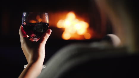 Woman-Drinking-Red-Wine-While-Sitting-By-The-Fireplace-Rear-View